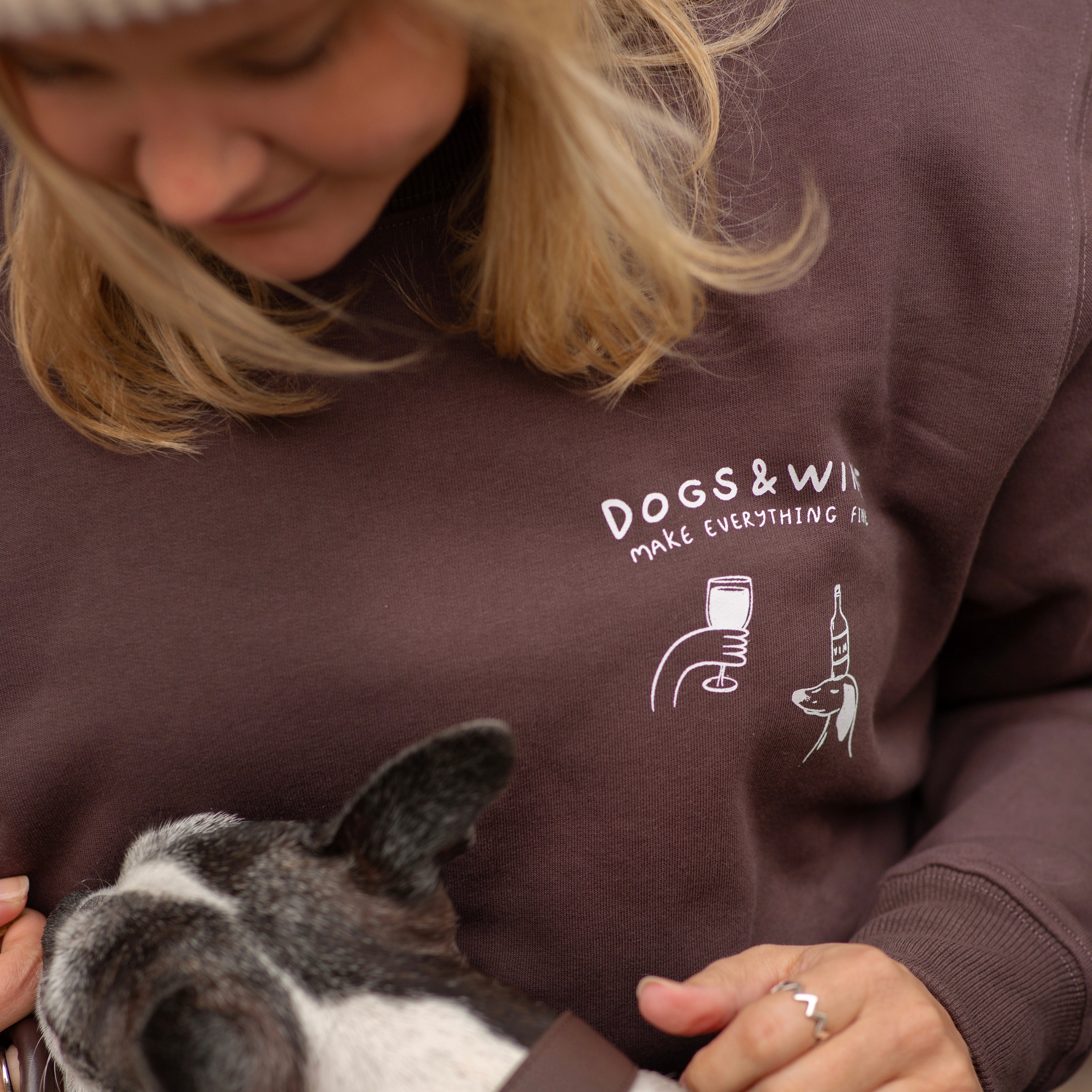Person wearing a sweatshirt with 'DOGS & WINE' text and graphic, holding a dog.