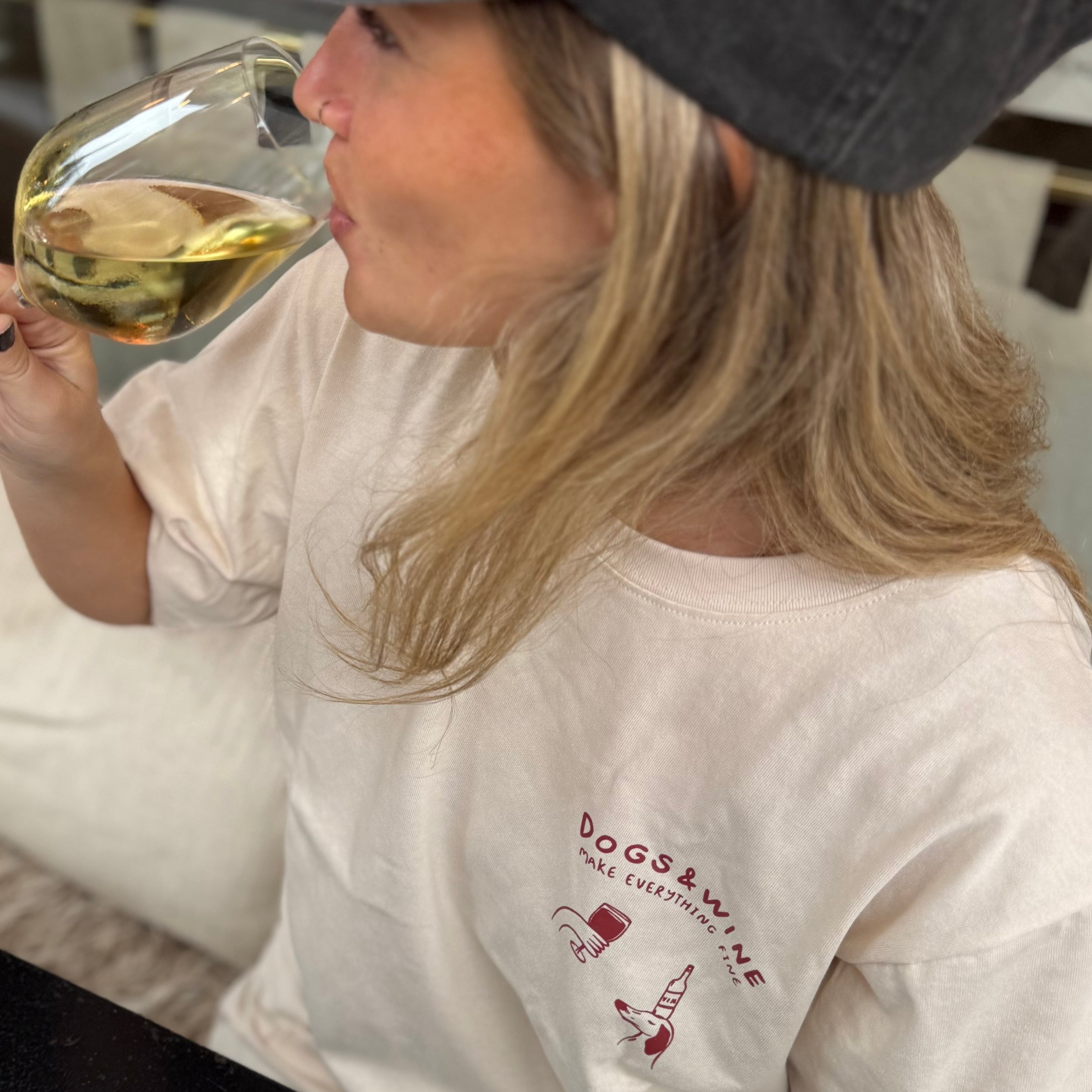 Person wearing a white t-shirt with 'DOGS & WINE' text, holding a glass of wine.
